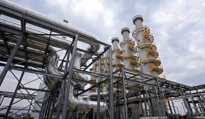 Large silver pipes next to white cylindrical towers against a cloudy sky