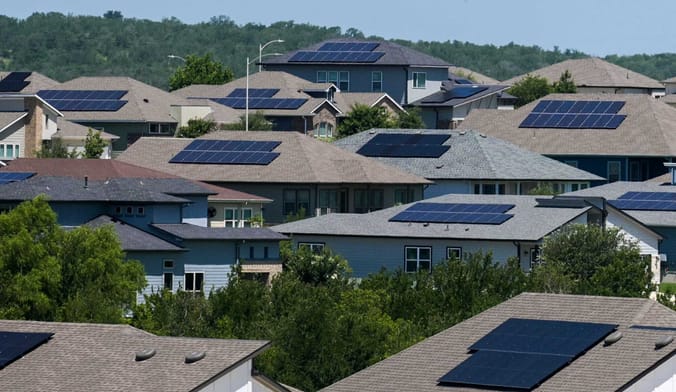House roofs with solar panels rise above treetops