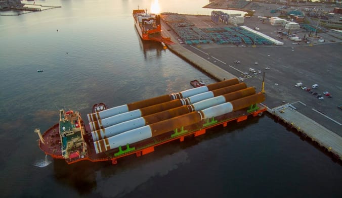 Aerial shot of wind turbine parts on a vessel at a waterfront yard at sunset