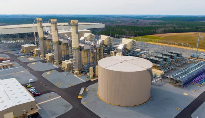 Aerial shot of industrial facility with numerous cylindrical towers, against a backdrop of forested hills