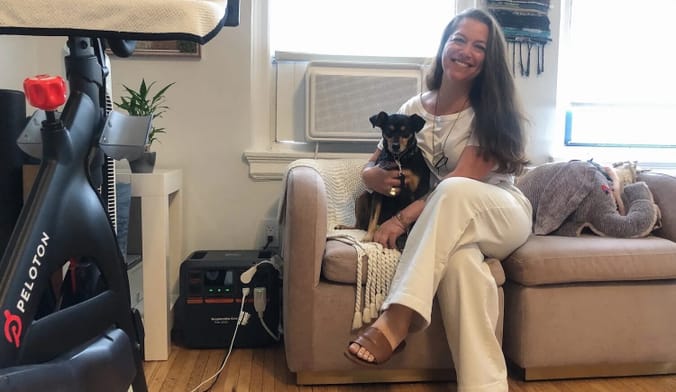 A woman and a dog sit on a couch near a small black box.