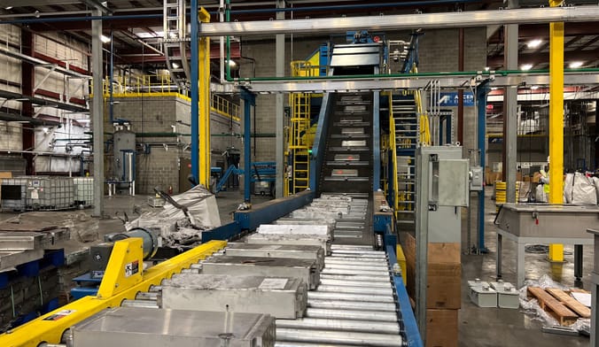 EV batteries are transported on a conveyer belt inside a large industrial facility