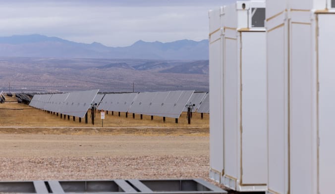 Rows of solar panels in California's Mojave Desert with battery storage installations in the foreground