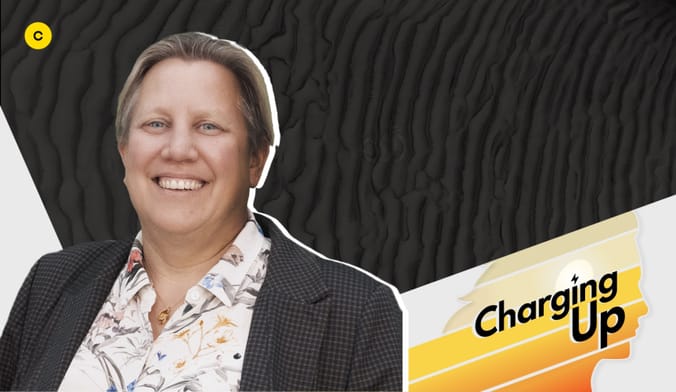 A smiling woman with short light-brown hair and a light skin tone wearing a gray blazer. A graphic overlay reads Charging Up.