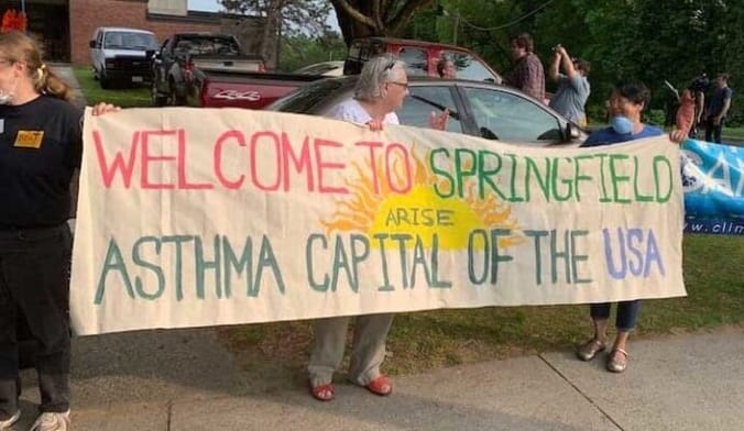 Community members holding a banner reading "Welcome to Springfield the Asthma Capital of the USA"
