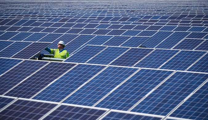 A worker in a hard hat stands amid rows of solar panels