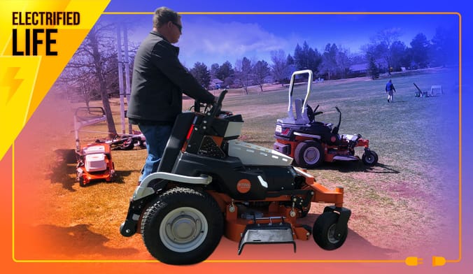 Man in grey pullover aboard electric stand-on mower at a park with grass and exposed soil and other electric lawn tools.