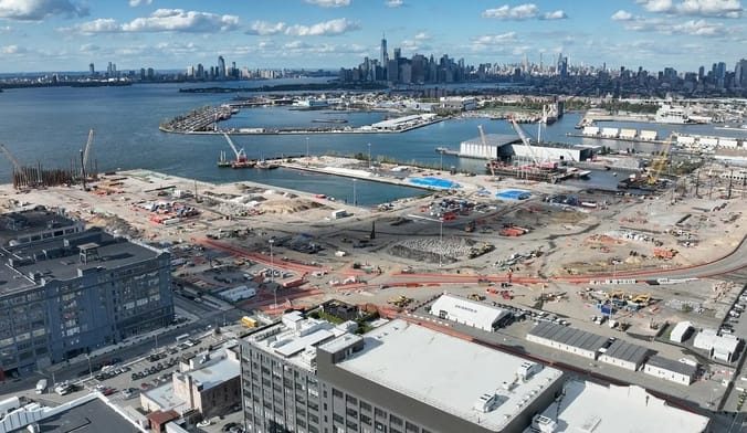 An industrial waterfront area under construction with a city skyline in the background.