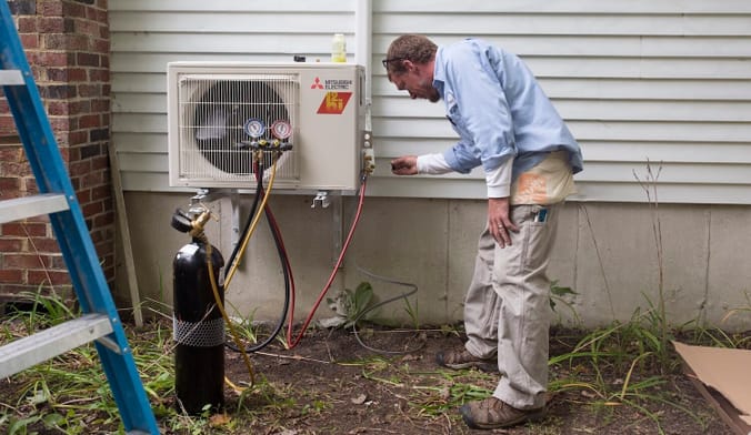A person bends down to look at HVAC equipment installed on the outside of a home.