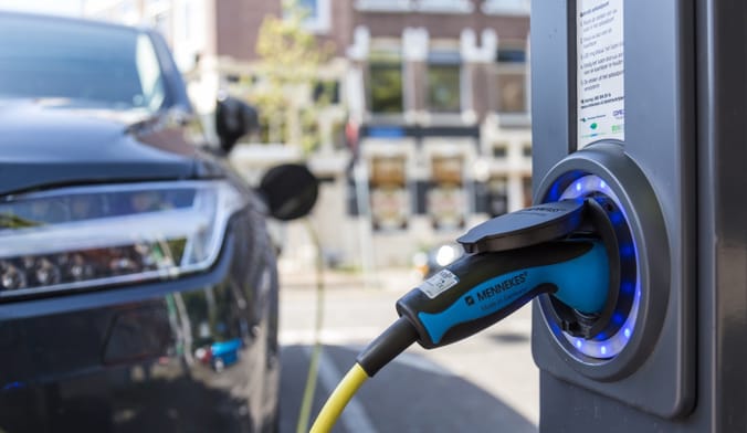 Close up of an EV charger with a car in the background