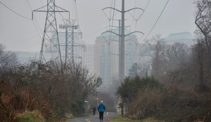 People walk along a paved path lined by transmission lines and trees on a misty day