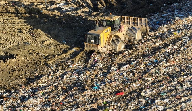 a yellow dump truck in a dirt pit with scattered trash