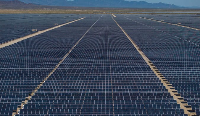 Solar panels stretching across the desert, mountains and blue sky in the distant background