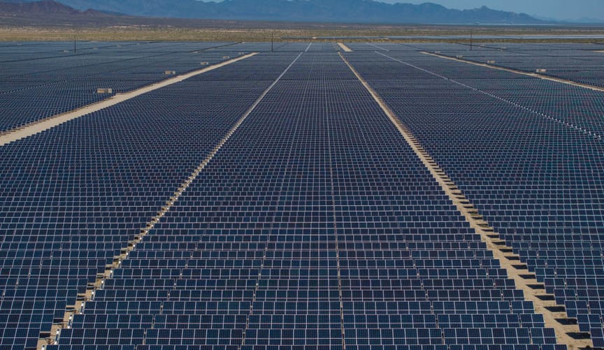 Solar panels stretching across the desert, mountains and blue sky in the distant background
