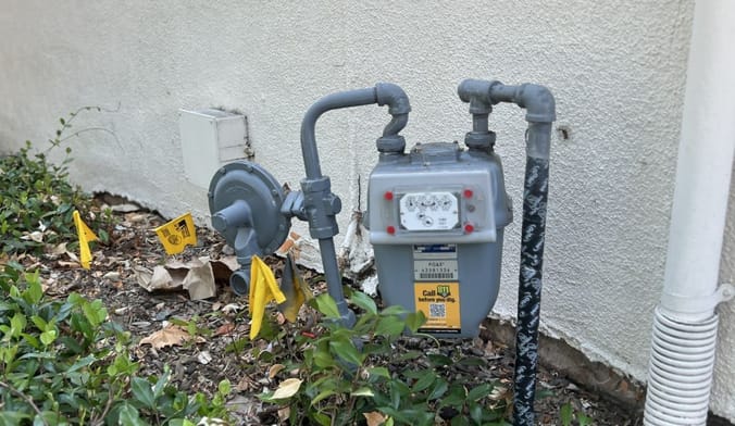 Pacific Gas and Electric (PGE) gas meter and utility infrastructure against a building wall