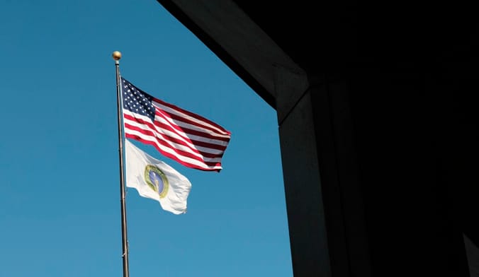Two flags fly against a blue sky.