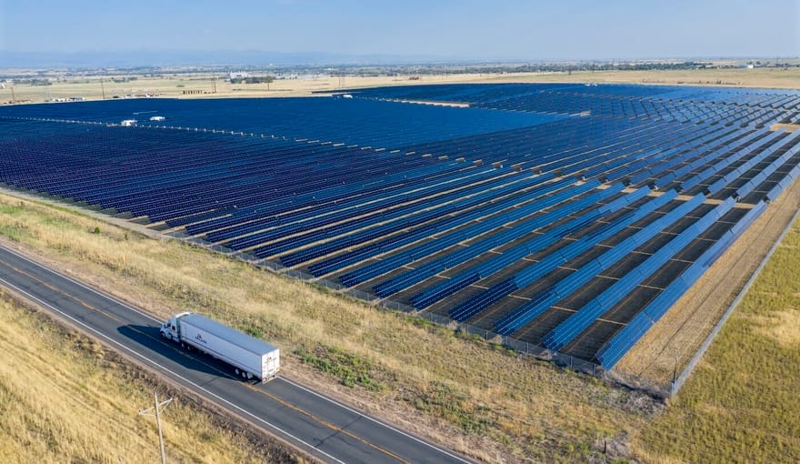Aerial view of solar panels in a field next to a road with a truck driving on it