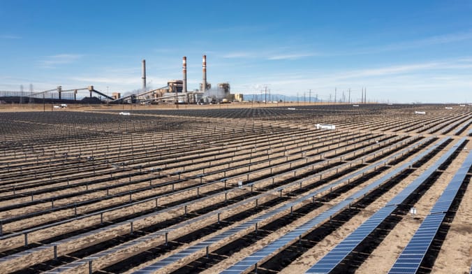 Aerial shot of rows of solar panels in a field by a large factory