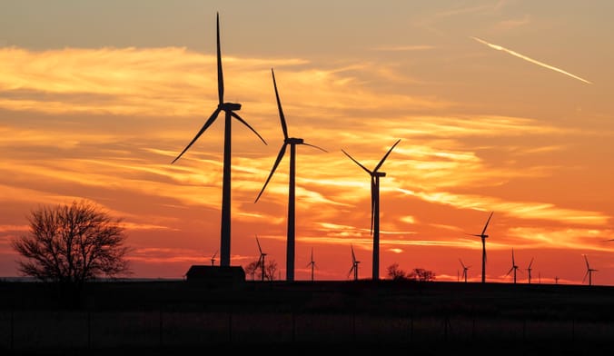 Turbine silhouettes rise against a sky at sunset in a rural landscape