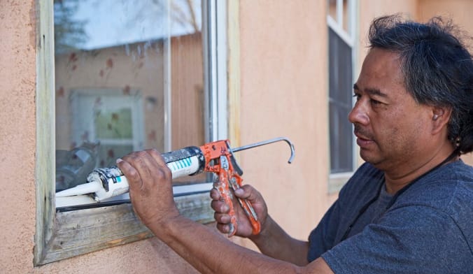 A person uses a caulk gun to seal cracks on the edge of a home window
