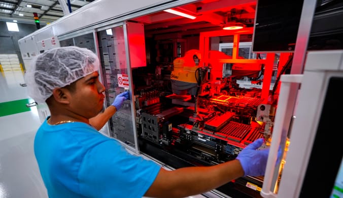 A person wearing a hairnet opens a machine with red lighting on the inside
