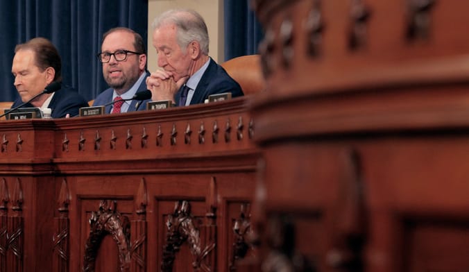Three people in suits sit behind a long wooden desk.