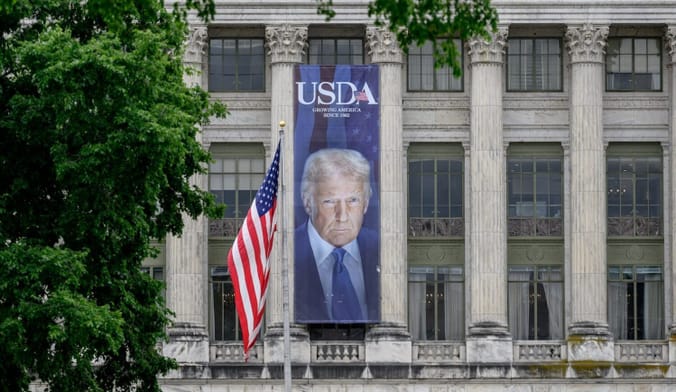 A large poster of Donald Trump's face under the words "USDA" hangs on the front of a government building