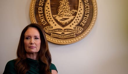 A woman stands in front of a wall with the U.S. Department of Agriculture seal on it