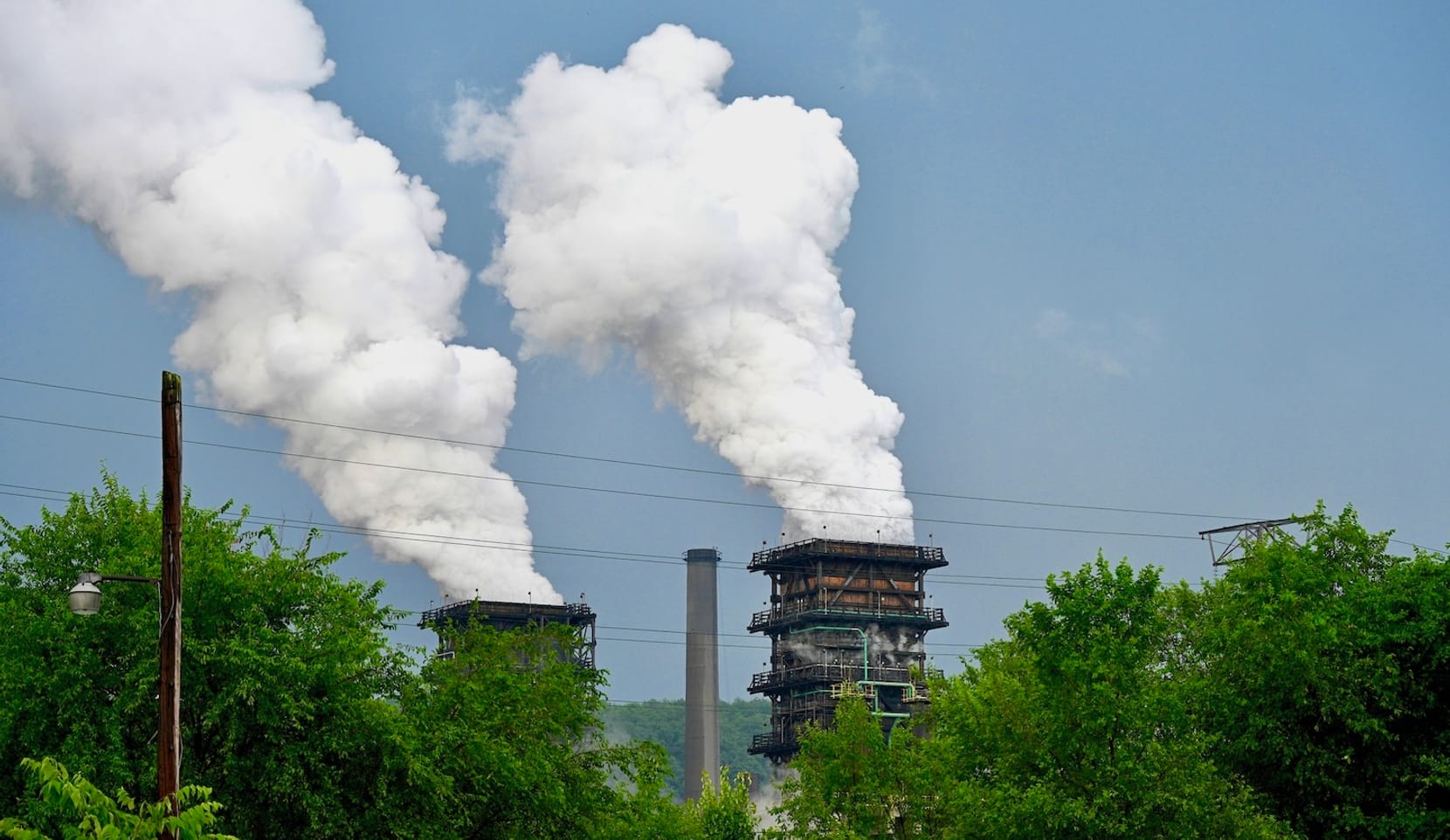 Pollution rises from two industrial towers seen rising above trees