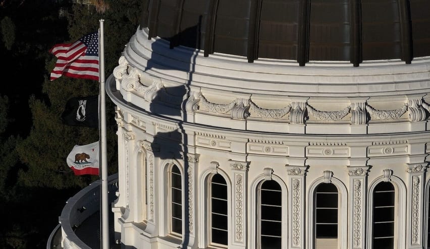 Government building with a domed top. Three flags fly on a pole on the building.