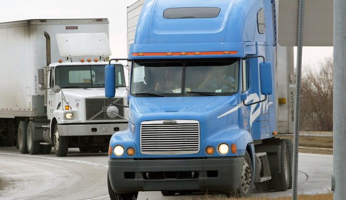 Two tractor-trailer trucks drive along a curving road.