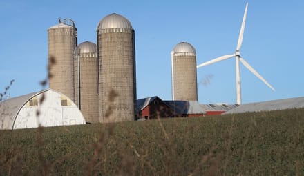 Silos and a barn next to a wind turbine on a sunny day