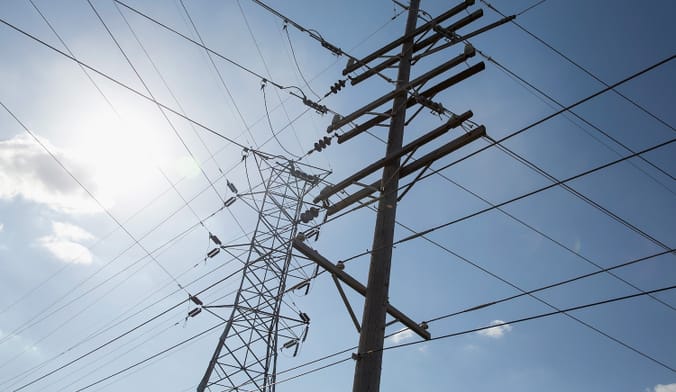 Transmission lines and poles silhouetted against a sunny blue sky.