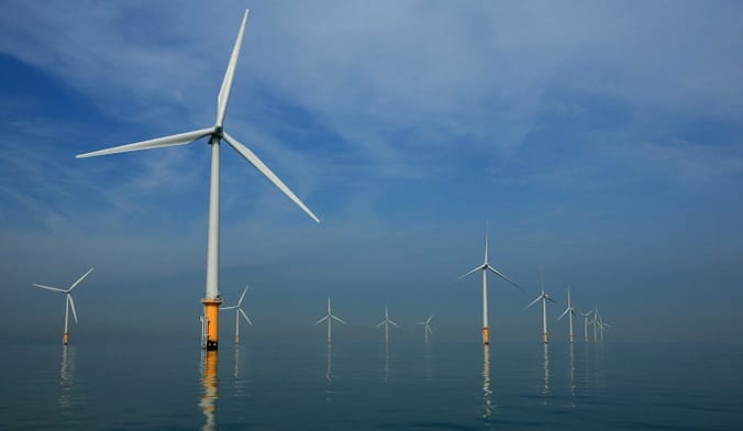 Wind turbines rise out of the water against a blue sky.