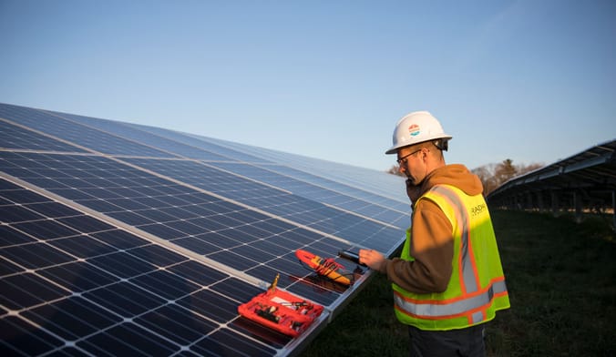 A worker examines a rooftop solar array against backdrop of blue sky