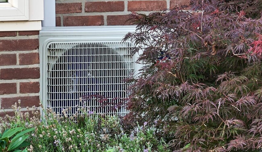 An HVAC equipment box on a brick wall behind plants