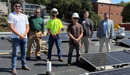 Six people stand on a roof with solar panels
