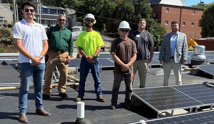 Six people stand on a roof with solar panels