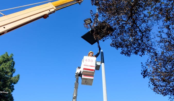 A person using construction equipment holds a light fixture on top of a pole