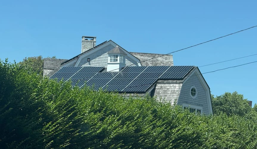 Solar panels on the roof of a house partially obscured by leafy bushes