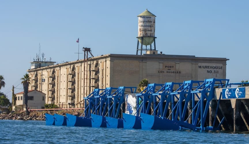 Blue steel structures sit in the water at a wharf with a warehouse on it