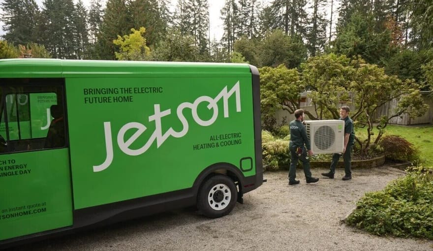 Two people carry HVAC equipment next to a truck that says "Jetson"
