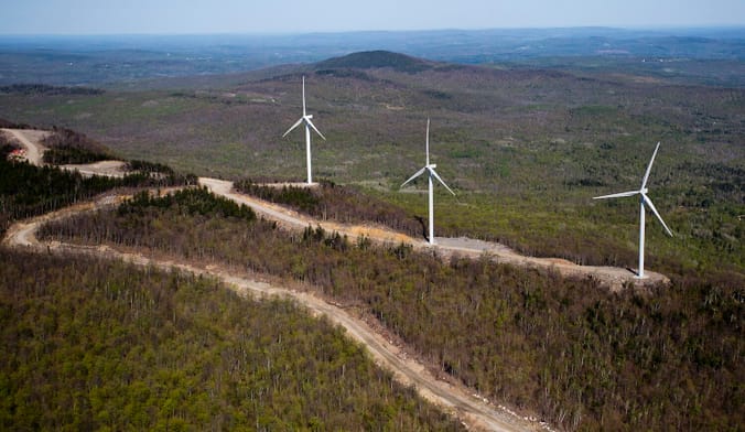 Aerial shot of three white wind turbines in a forested hilly landscape with several roads cutting through.