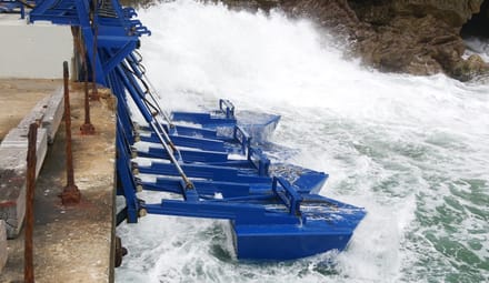 Waves crash against blue steel infrastructure on the coast
