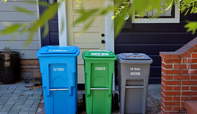 three blue, green, and gray bins in a row in front of a doorway of an urban home.