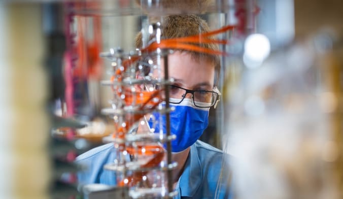 A person wearing a face mask and glasses viewed from behind scientific equipment.