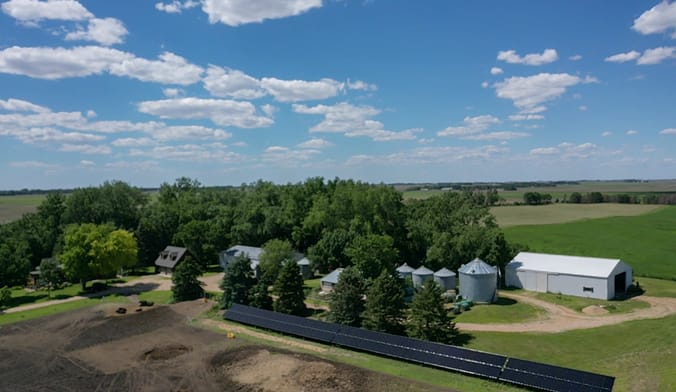 Aerial shot of fields, trees, a row of solar panels, and a barn