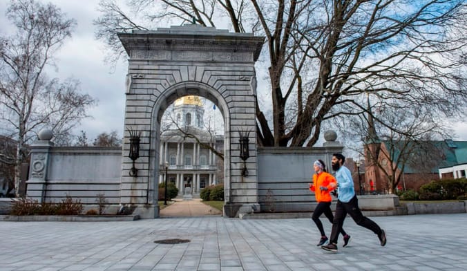Two people in winter athletic clothing run past a stone arch. Behind the arch is a building with pillars and gold dome
