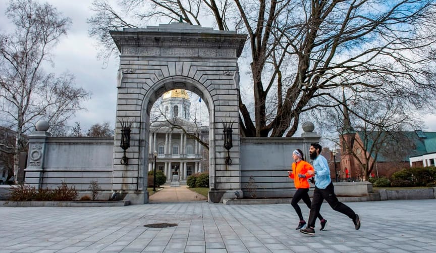 Two people in winter athletic clothing run past a stone arch. Behind the arch is a building with pillars and gold dome