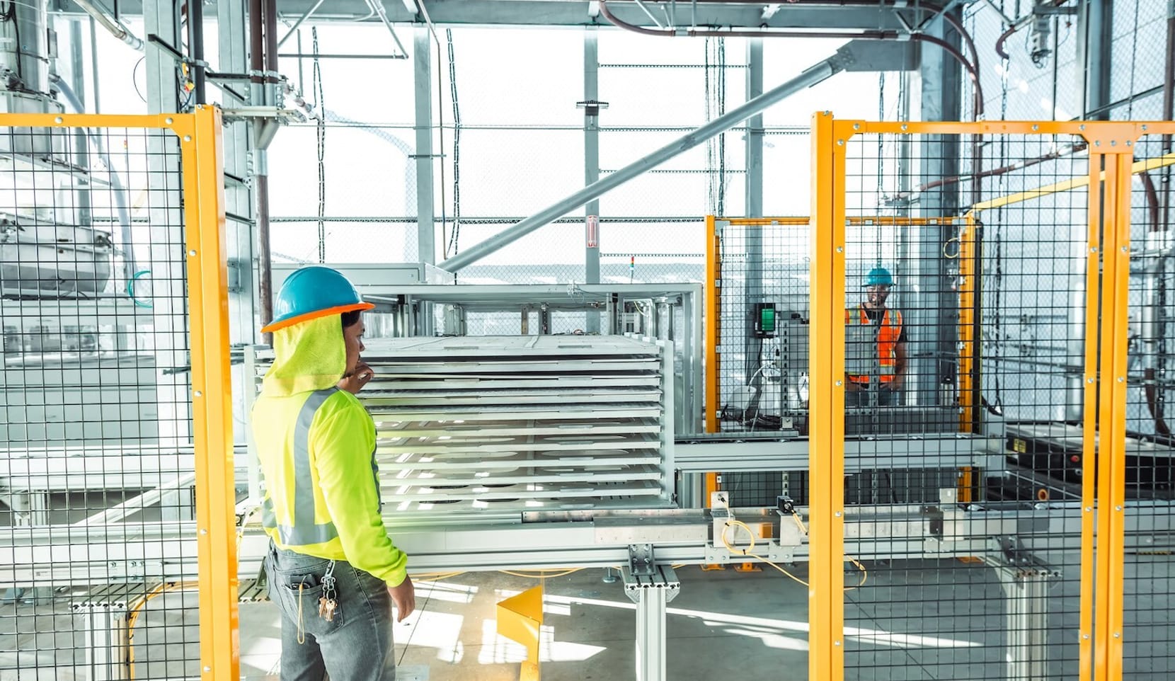 An employee in high-visibility safety gear and a hardhat stands in a production facility